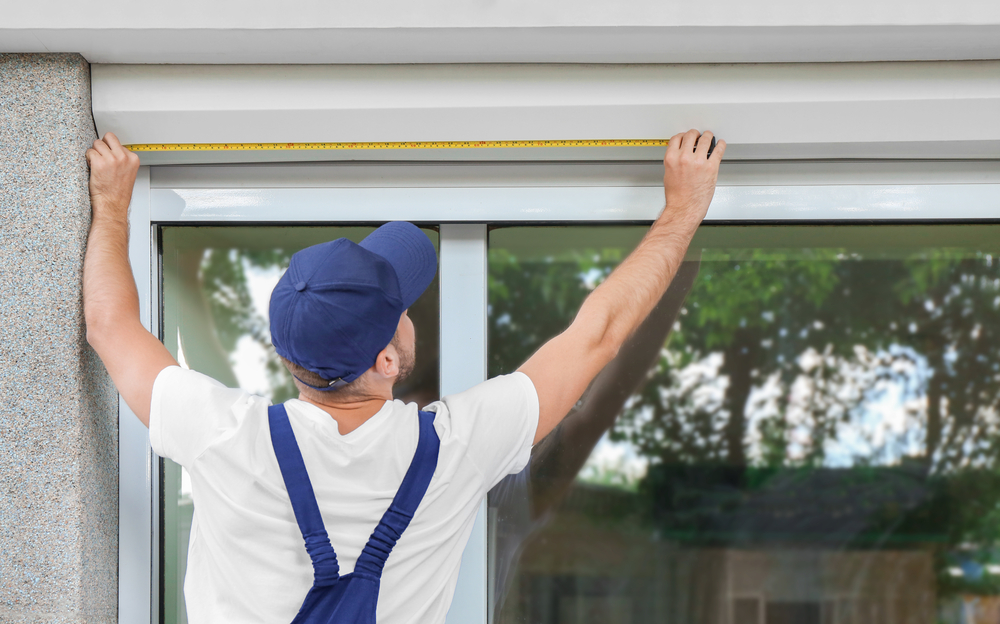image of a Man measuring window prior to installation of roller shutter outdoors